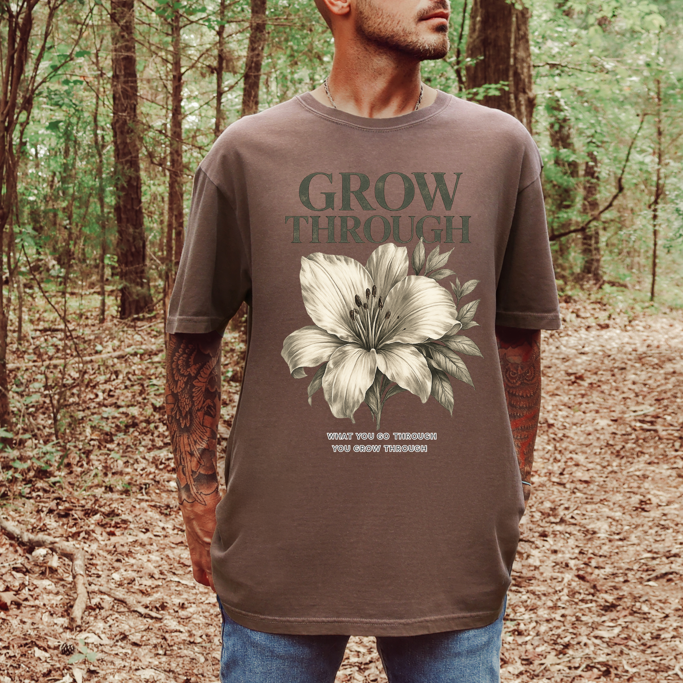 Person wearing a brown t-shirt with a floral design and text in a forest setting